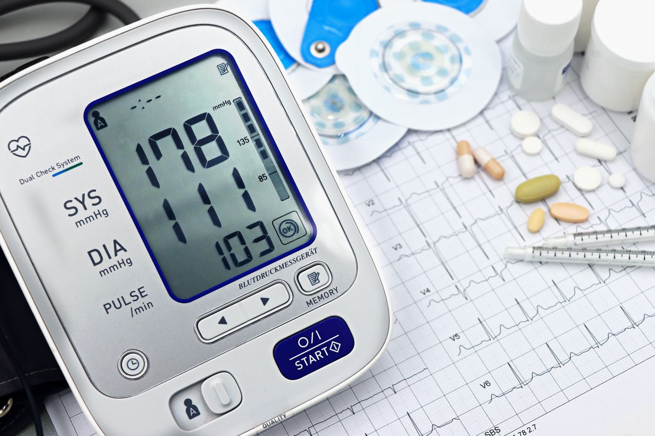 About Close-up of a digital blood pressure monitor with ECG printout, pills, and medical tools.