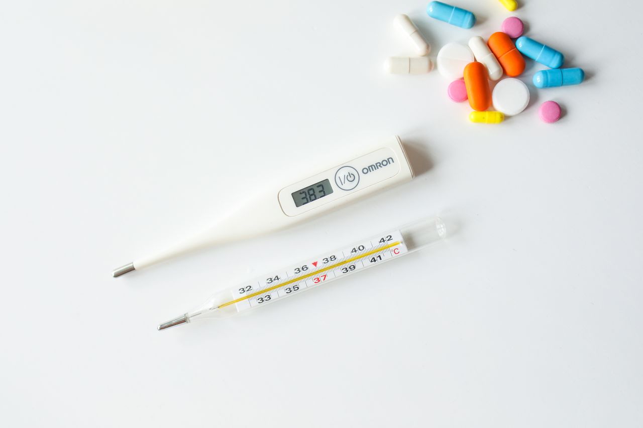 Digital and glass thermometers with colorful pills on white background.