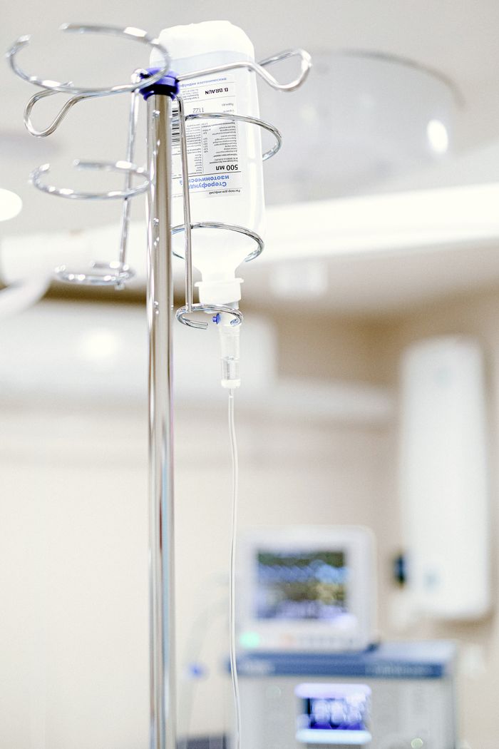 Home Close-up of an IV drip in a sterile hospital setting with background medical equipment.